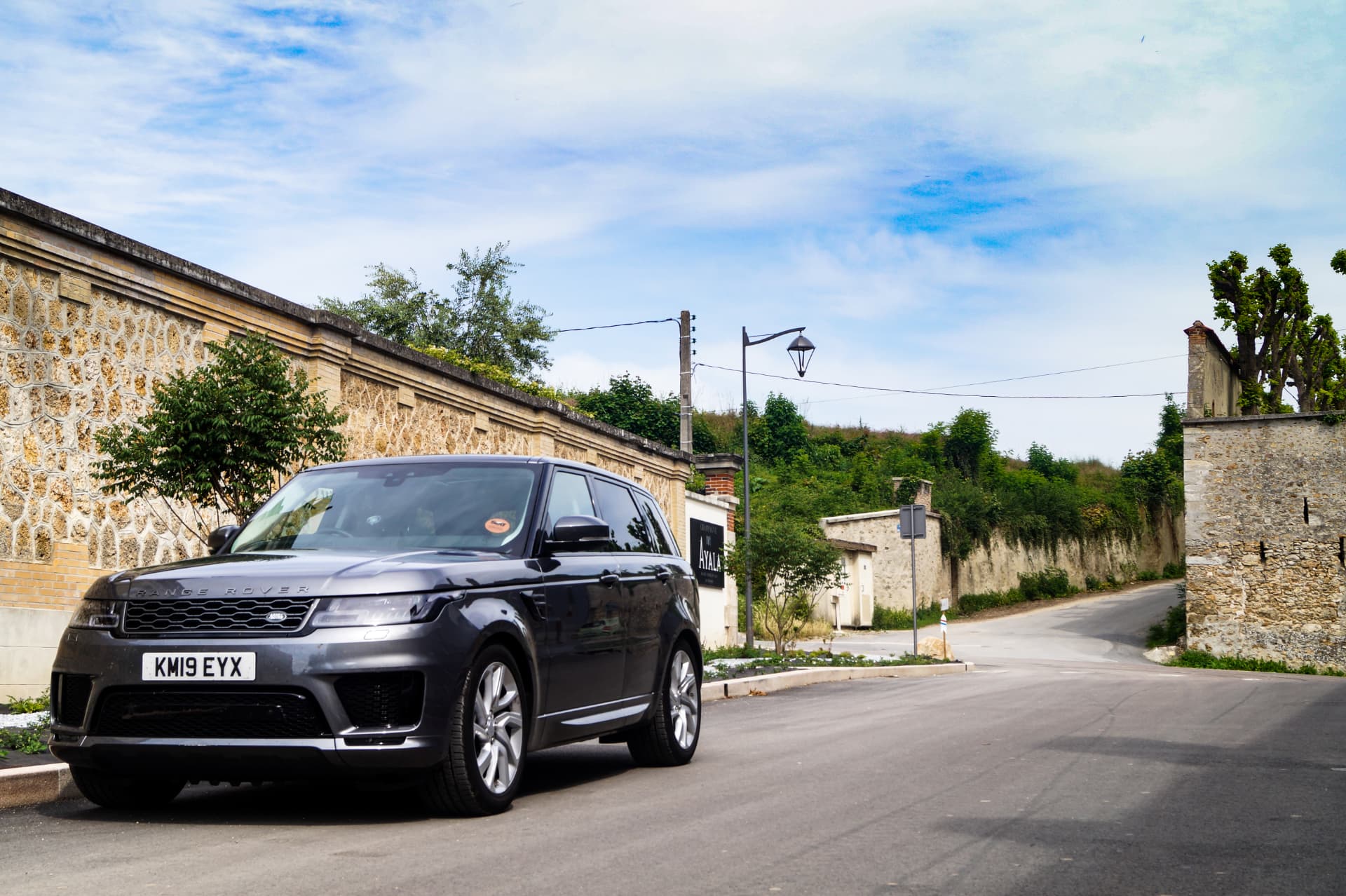 Range Rover parked on a quiet road beside a stone wall under a bright sky